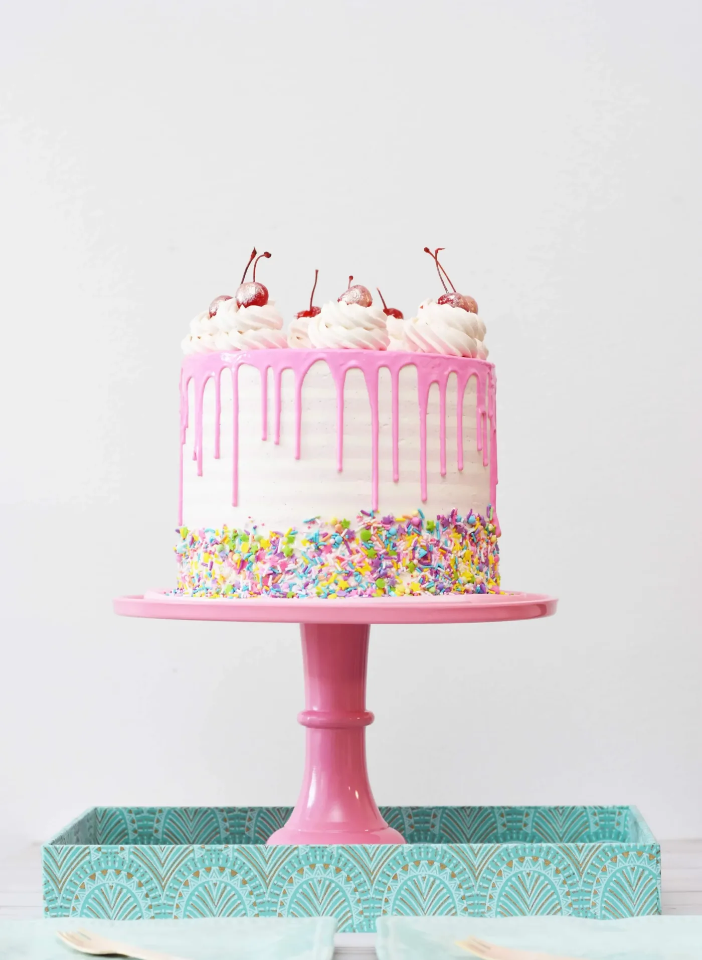 Rosa Drip-Torte mit bunten Streuseln auf rosa Tortenständer